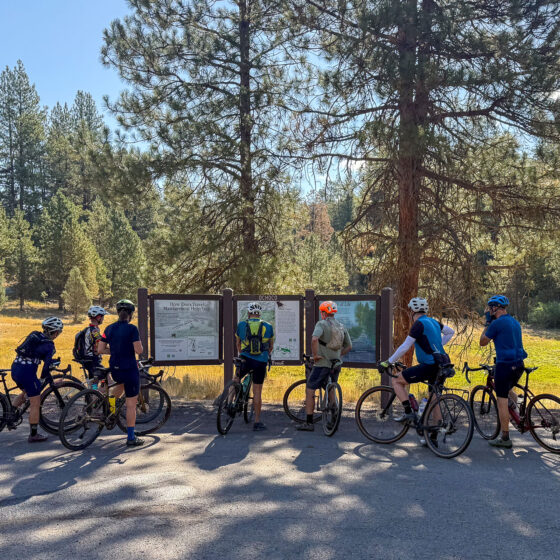 Group of cyclists at kiosk sign.