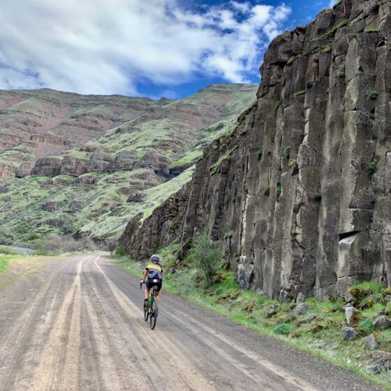 Cyclist on gravel road with basalt cliffs near the lower Deschutes River.