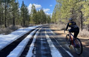 Gravel cyclist on Brooks Scanlon Logging road with some snow and ice in north facing sections in March.