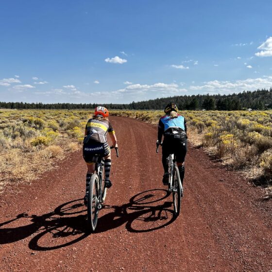 Two women cyclists on red cinder road.