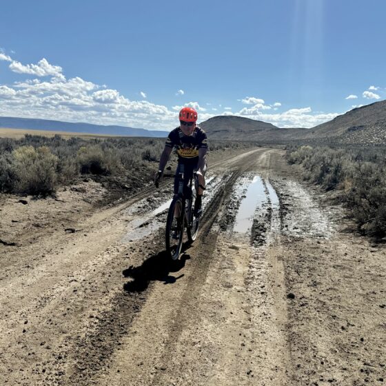 Gravel cyclist on dirt road with mud puddle.