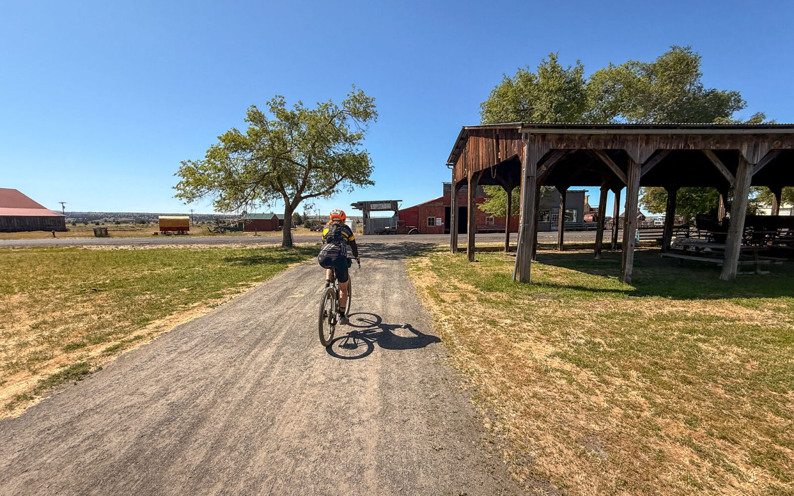 Cyclist riding past historic buildings on dirt road.